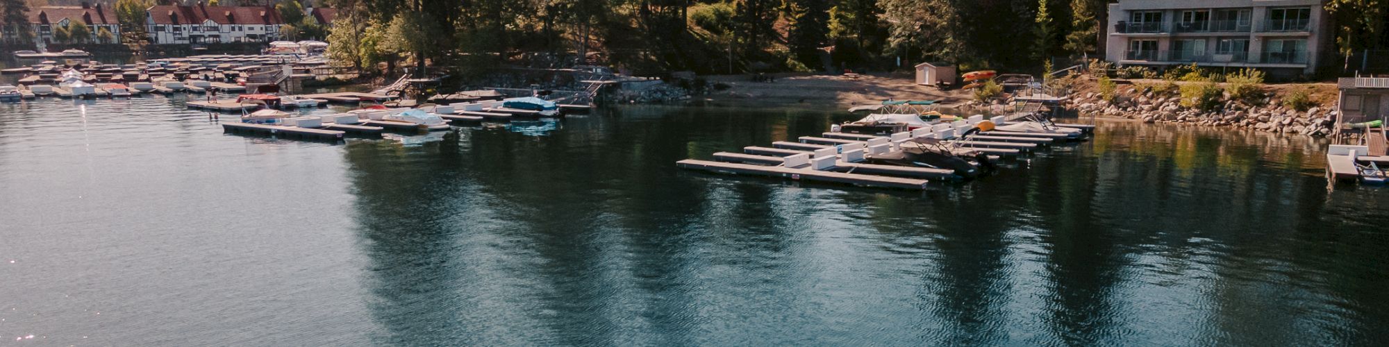 A calm lakeside marina with many docked boats and cabins, plus a red kayak paddler on the water.