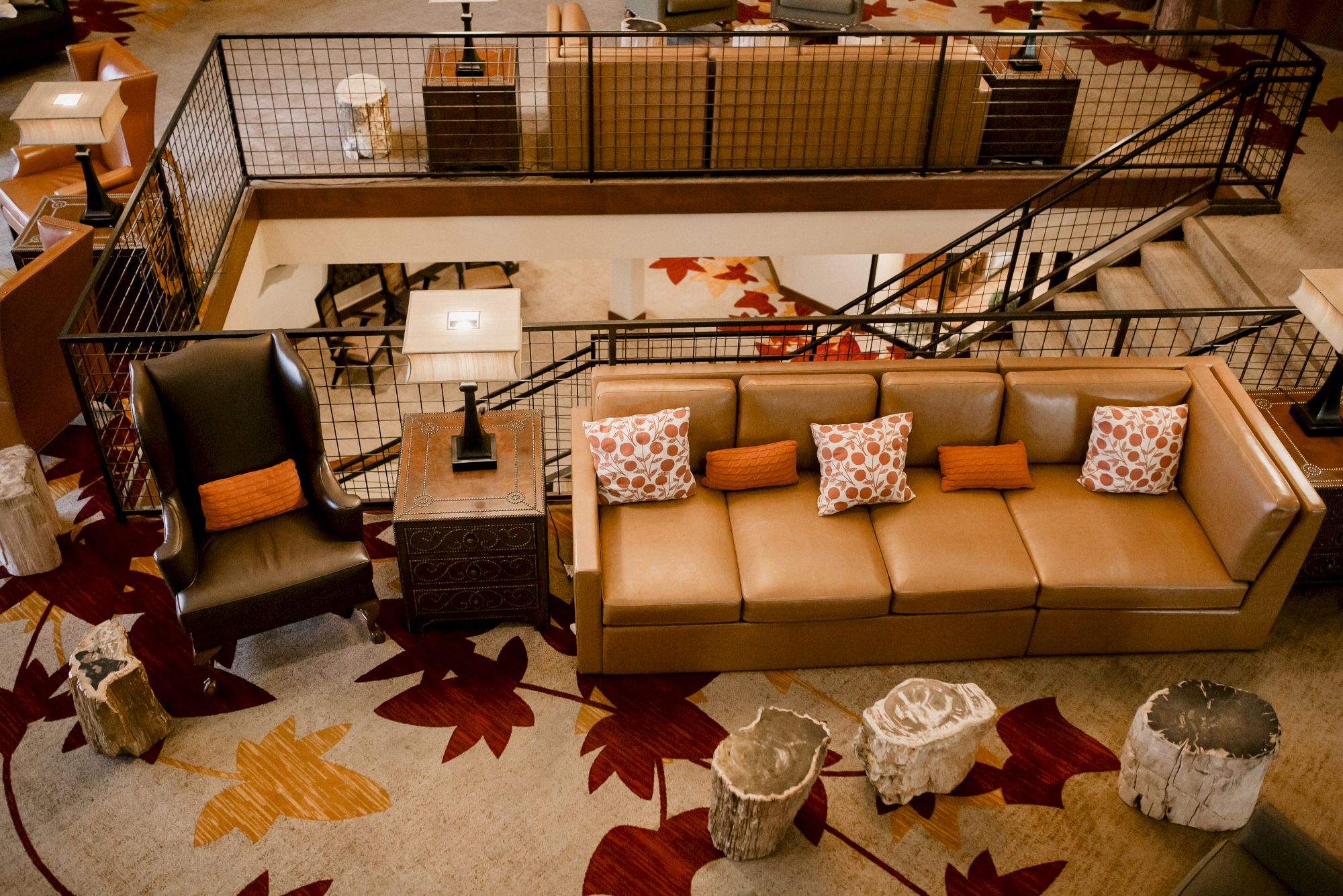 Cozy indoor lounge with tan sectional sofa, patterned cushions, two leather chairs, and a loft railing overlooking a lower level.