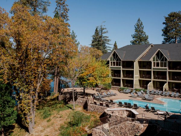 Sunlit resort courtyard with an outdoor pool, lounge chairs, and a multi-story building surrounded by autumn trees.