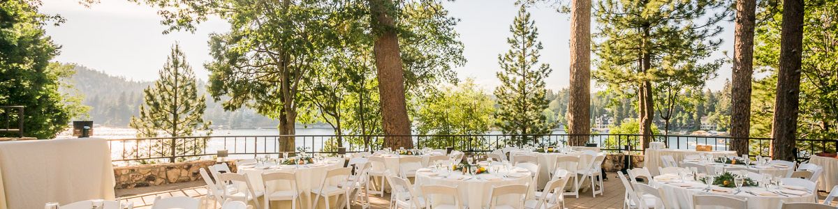 An outdoor wedding reception setup with white tablecloths, chairs, glassware, and golden trees under sunny skies.