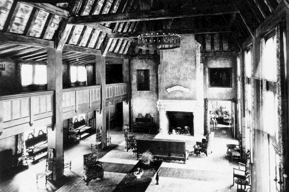 Vintage photo of Lake Arrowhead's Great Hall with a fireplace, timber beams, and sofas.