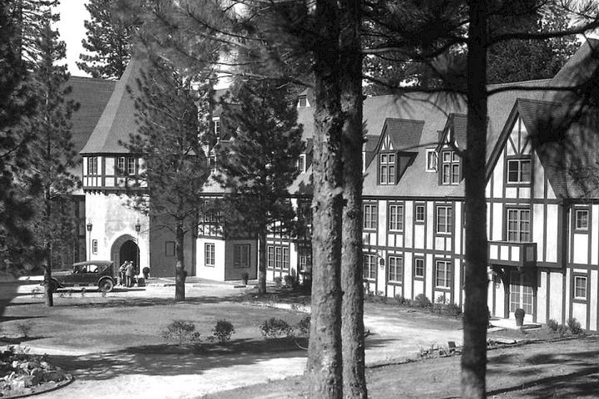 Vintage image of Lake Arrowhead's Tudor-style buildings with archway, surrounded by pine trees
