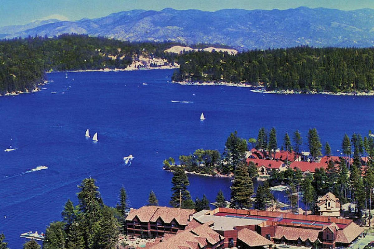 Historic aerial view Lake Arrowhead with boats, surrounded by forest and mountains.