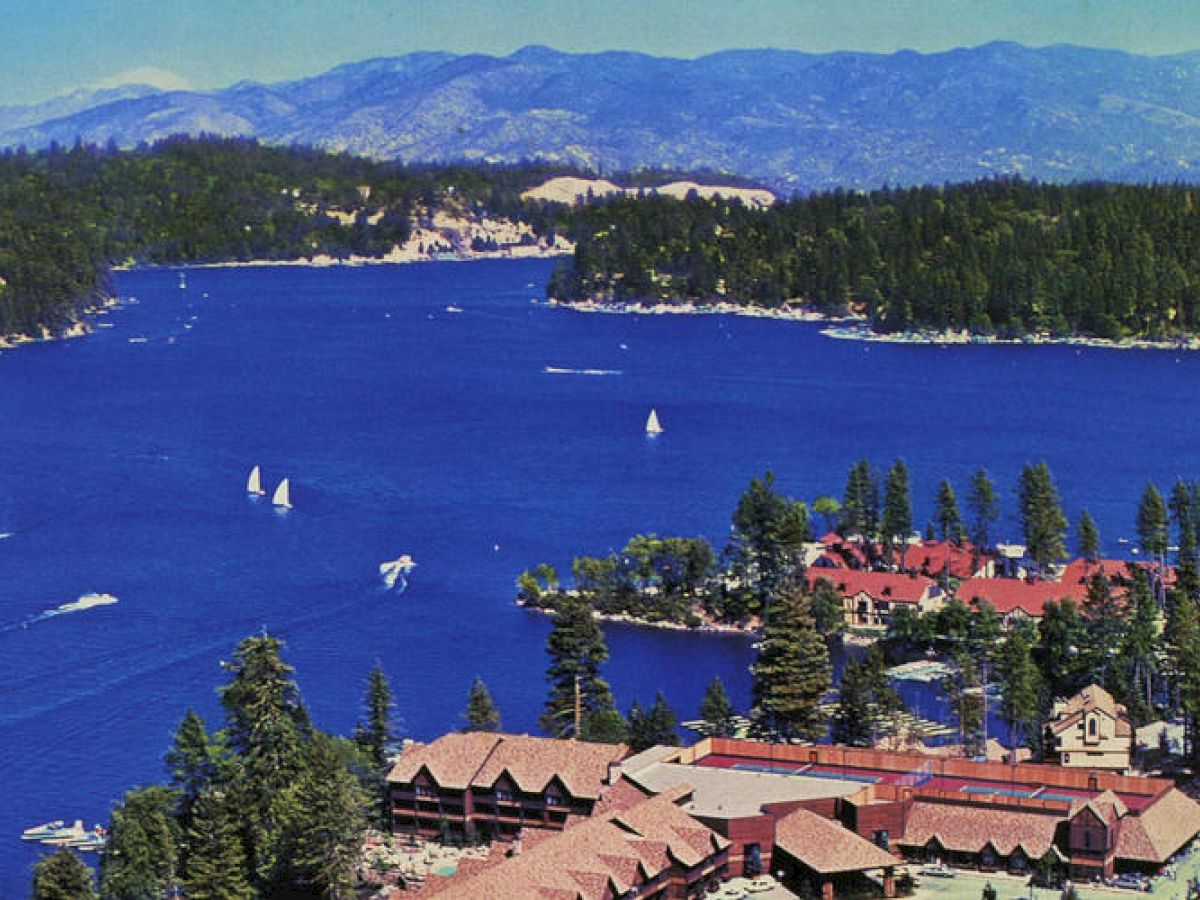Historic aerial view Lake Arrowhead with boats, surrounded by forest and mountains.
