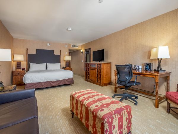 A hotel room with a large bed, wooden dresser, TV, lamps, and a desk with chair.