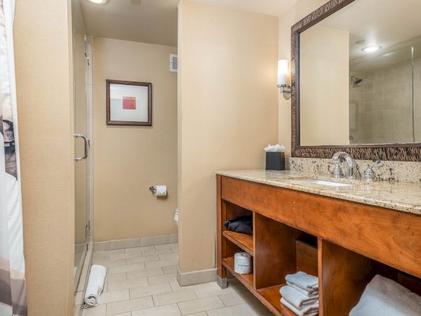A modern bathroom with a glass shower, toilet, and a granite sink vanity with towels and a lit mirror.