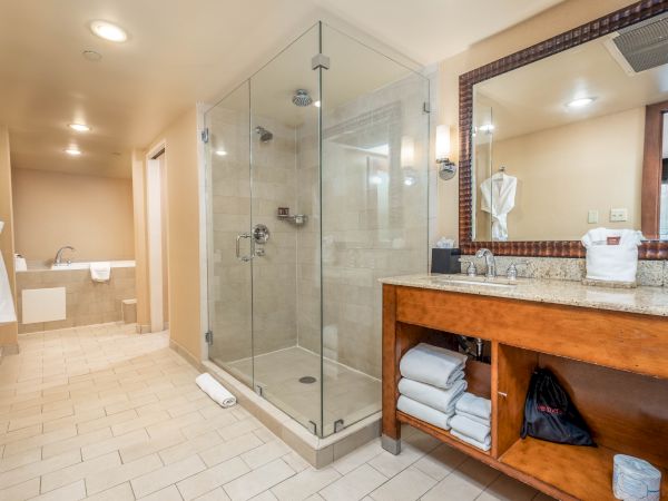 A modern bathroom with a glass shower, tiled floor, and a vanity mirror above a granite sink with folded towels.