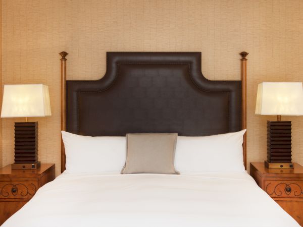 A hotel-style bed with a dark tufted headboard, white pillows, two matching nightstands, and lit table lamps on each side.