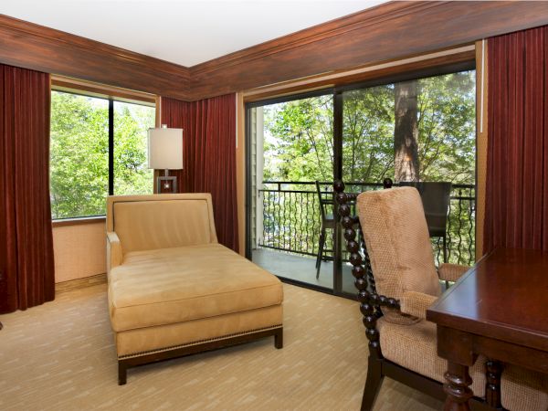 Cozy hotel room with a bed, warm curtains, and a view through sliding glass doors onto a tree-filled balcony.
