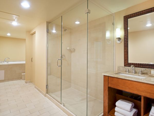 A modern bathroom with a tiled shower, glass enclosure, and a granite vanity with mirror and sink.