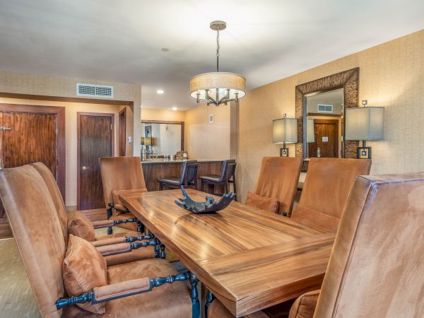 A hotel meeting room with a large wooden table, leather chairs, pendant chandelier, and warm wood-paneled walls and doors.