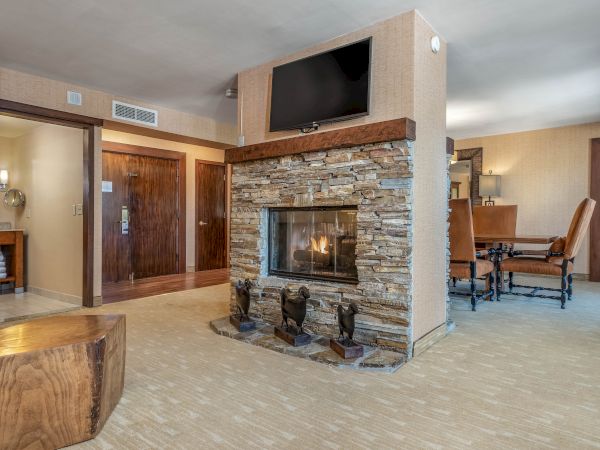 A living room with a stone fireplace, mounted flat-screen TV, wooden doors, and seating by the hearth, with decorative figures.