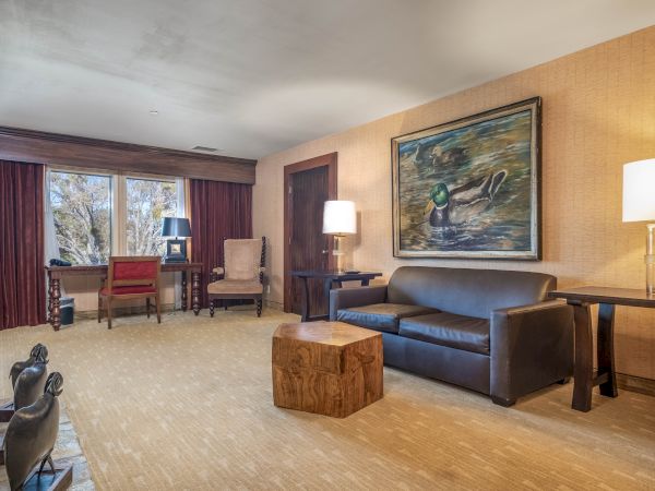A cozy living room with a blue sofa, chairs, coffee table, lamps, and a framed duck painting on a textured wall.