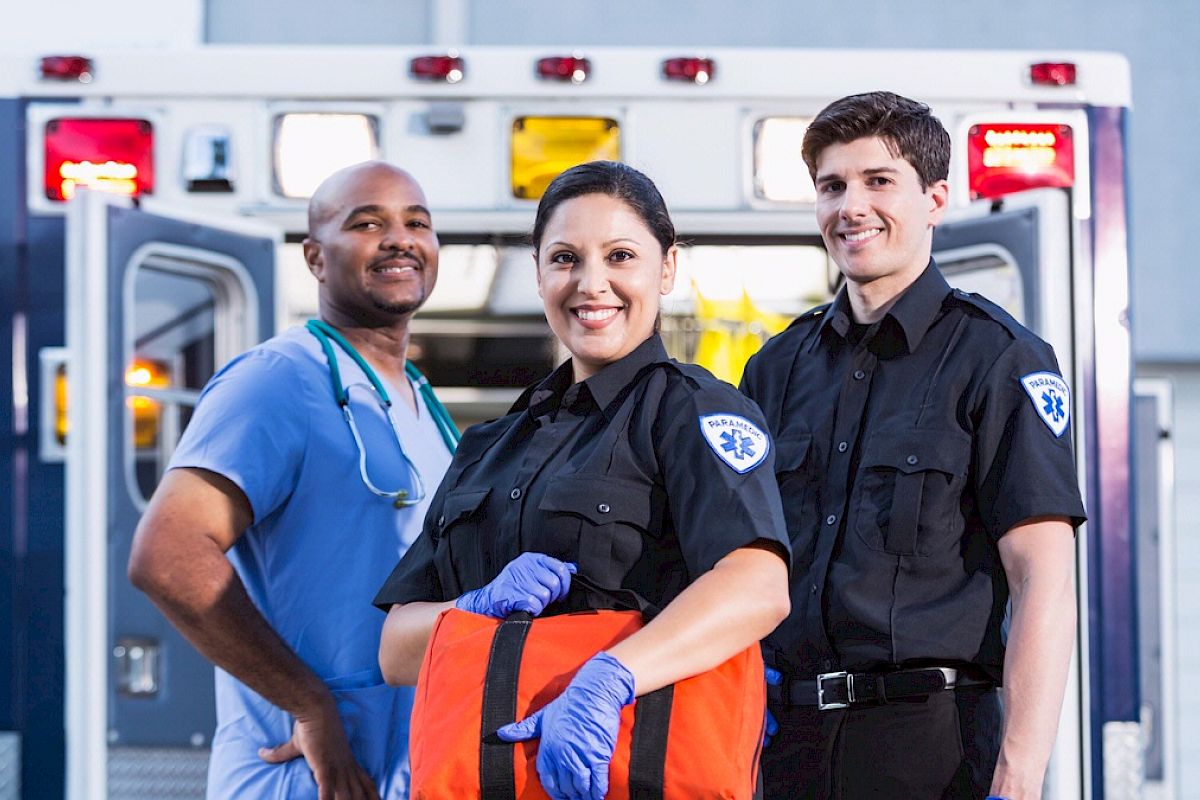 The image shows three emergency medical personnel standing in front of an ambulance, smiling, and ready for action, ending the sentence.
