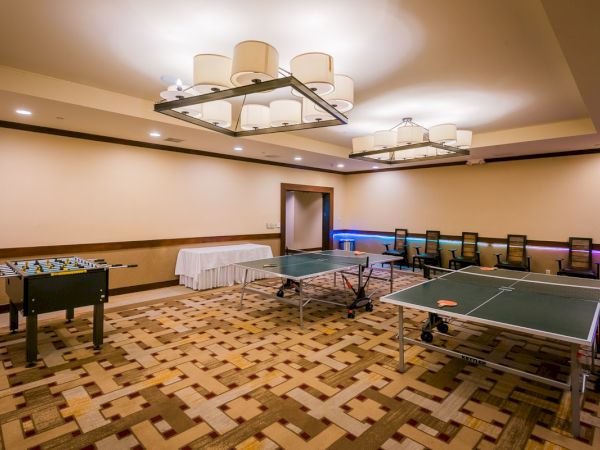 A game room with a ping pong table, foosball, carpeted floor, and overhead lighting.