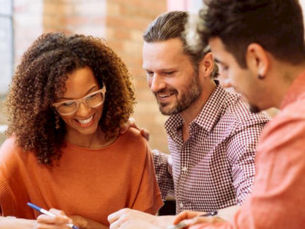 Three people are collaborating over a document, engaged and smiling.