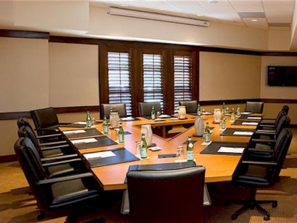 A well-lit boardroom with a large table, chairs, and notepads for a meeting.