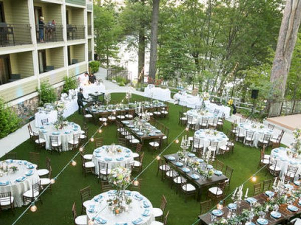 Outdoor event setup with tables and chairs on a lawn, surrounded by trees and a building.