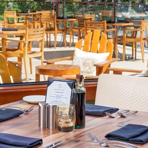 An outdoor restaurant patio with neatly set tables, wooden chairs, and cutlery&mdash;ready for a meal in the sunshine.
