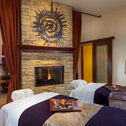 Cozy bedroom lounge with a stone fireplace featuring an abstract metal sun motif, brown curtains, and hanging white robes.