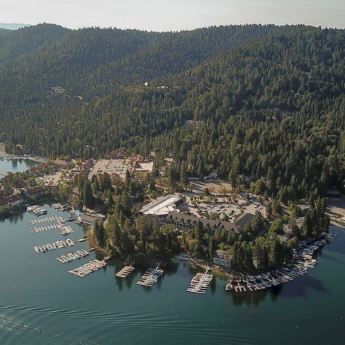 An aerial view of a lakeside resort with marinas, many docked boats, and dense green forest hills around it.