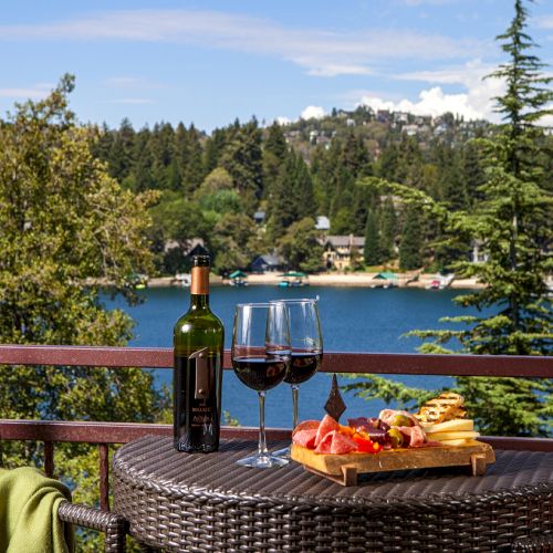A scenic lakeside patio with a bottle of wine, two glasses, and a charcuterie board overlooking the water.