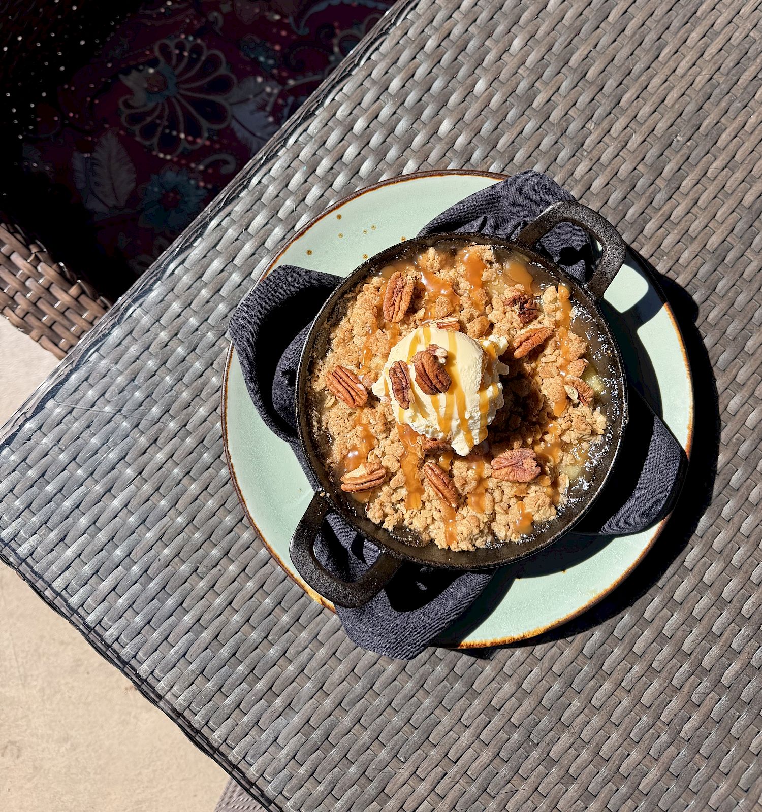 A skillet apple crumble dessert with vanilla ice cream, caramel-like sauce, and chopped pecans on a plate.
