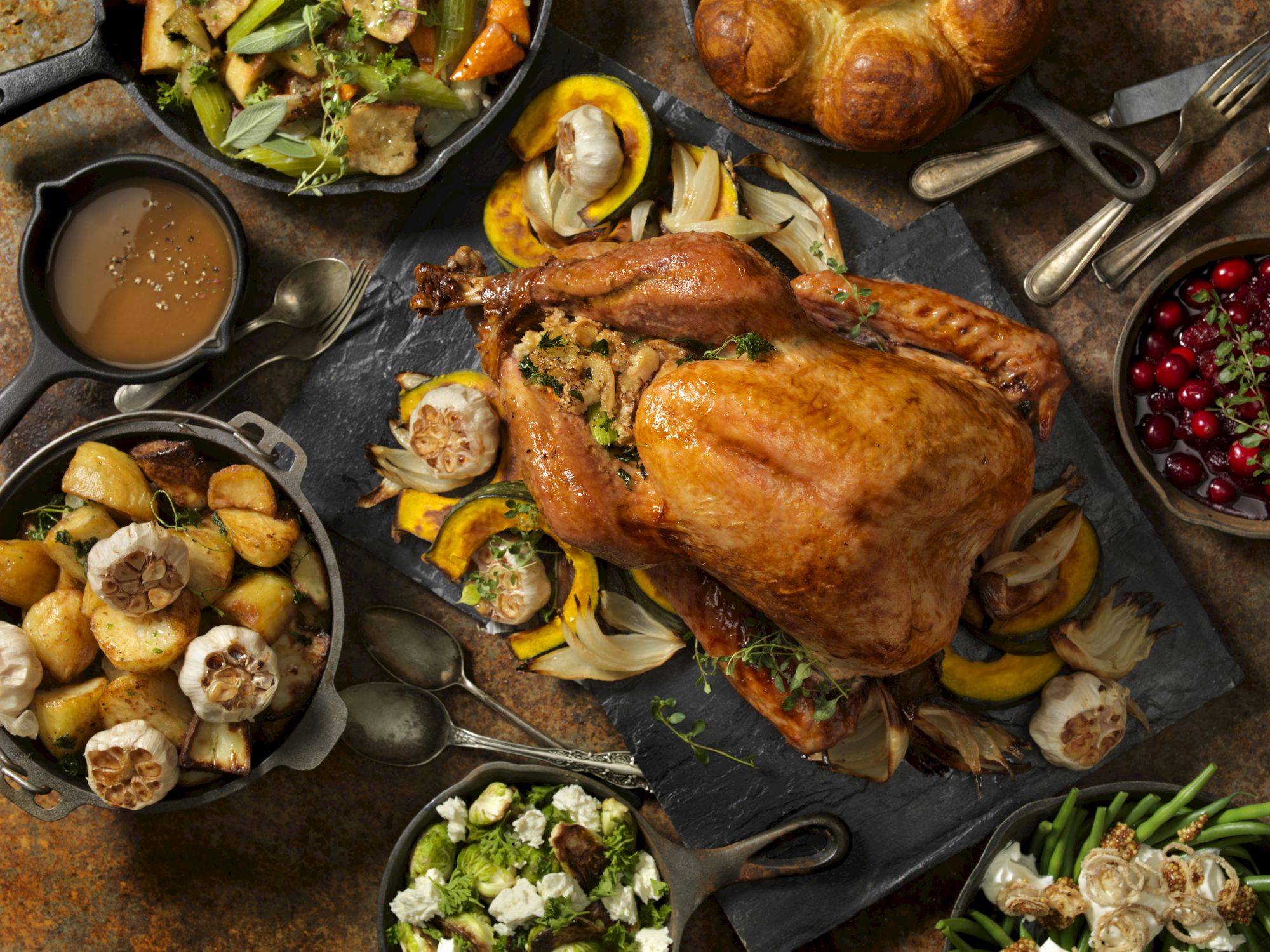 Roasted turkey with roasted vegetables, garlic, gravy and cranberries on a rustic slate, ready to serve.