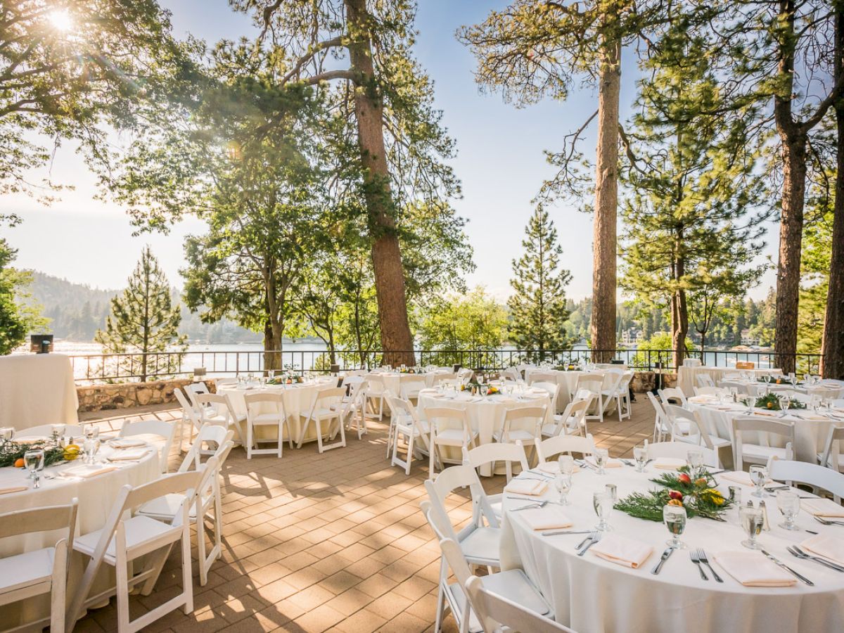 Outdoor event setting with white chairs and tables, near trees with a lake view.