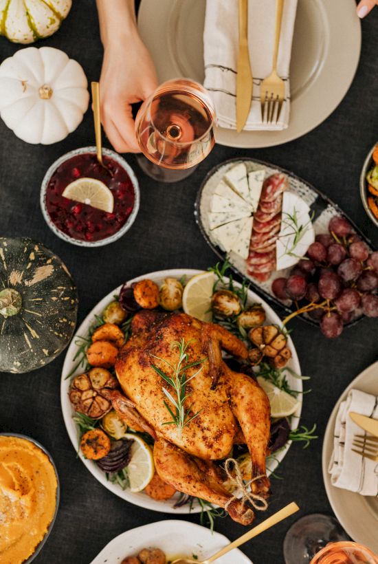 An overhead feast: roasted turkey and veggies on plates, grapes and lemon slices, plus glasses of red and ros&eacute; wine.