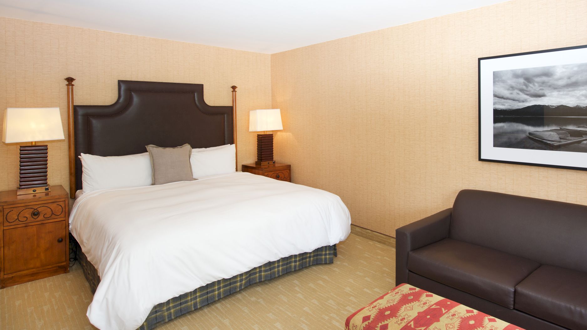 A tidy hotel room with a large bed, bedside lamps, a small couch, and a framed landscape photo on the wall.
