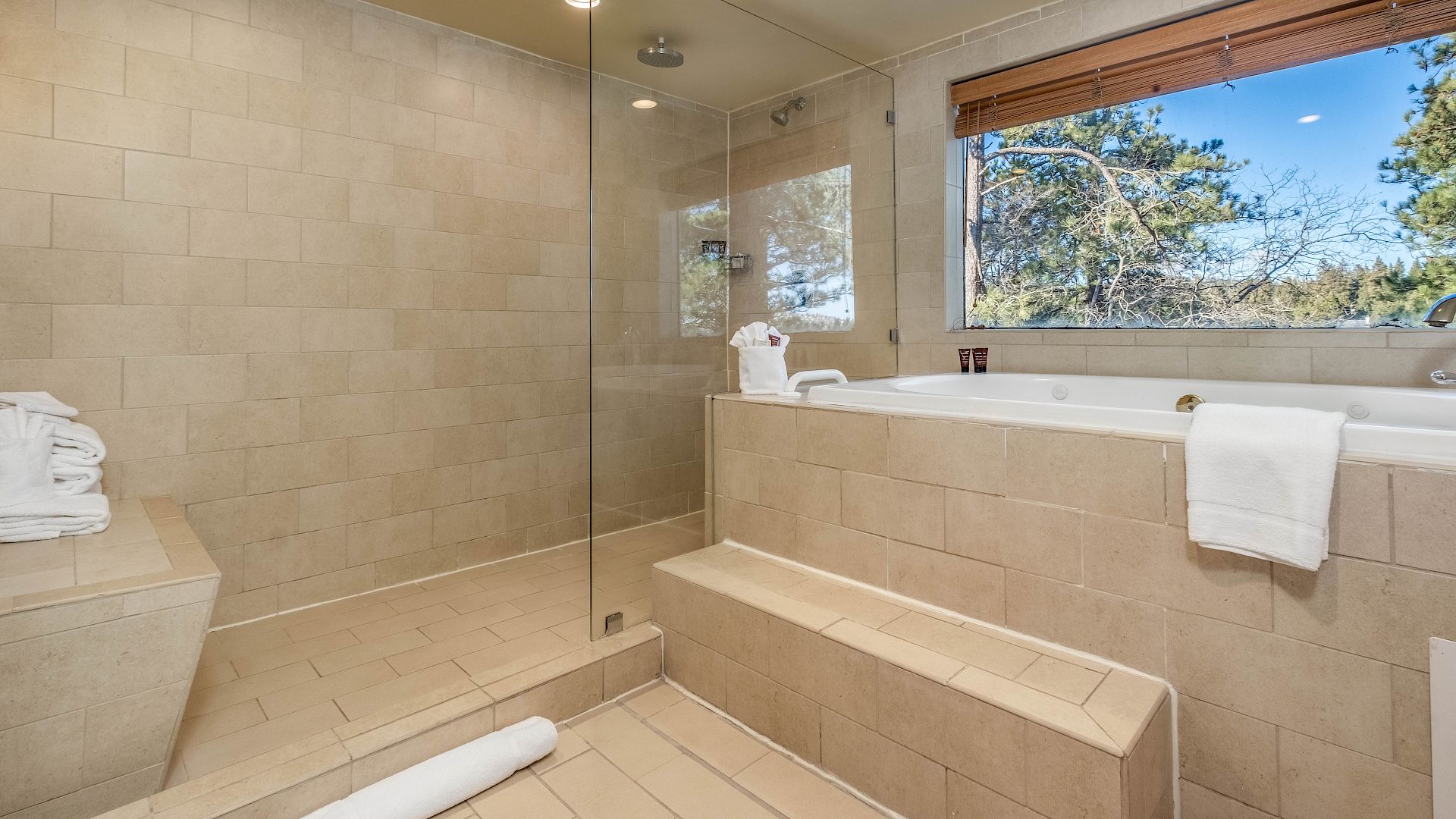 Modern bathroom with tiled walk-in shower, glass door, bathtub, and neatly folded towels under bright ceiling lights.