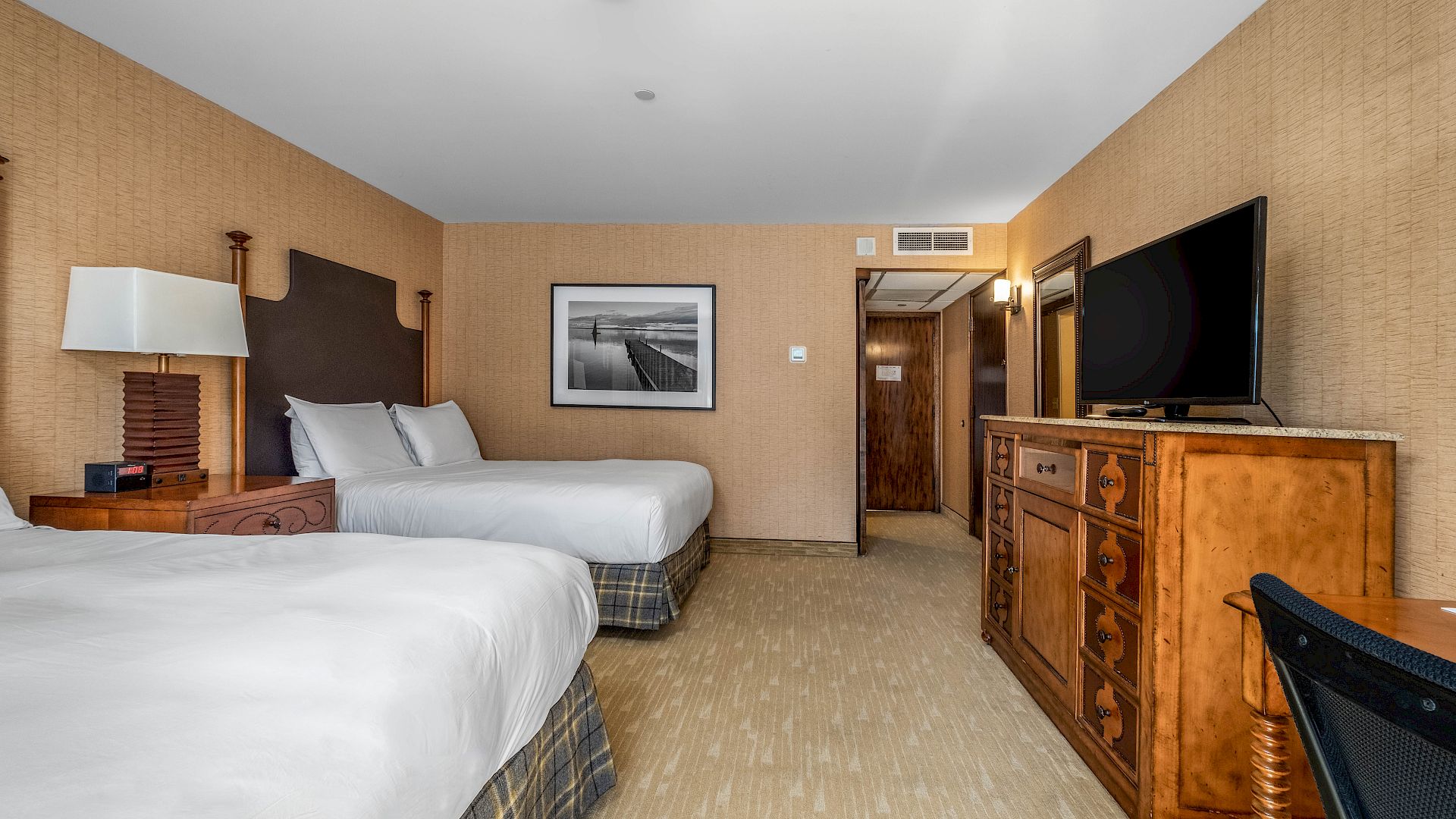 A hotel room with two beds, a dresser and large mirror, framed art, and warm lighting.