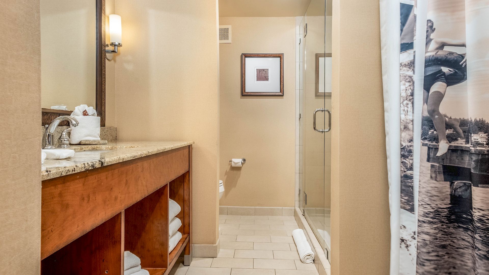 Modern hotel bathroom with a marble vanity, towels, mirror, and a glass-enclosed walk-in shower with shower curtain.