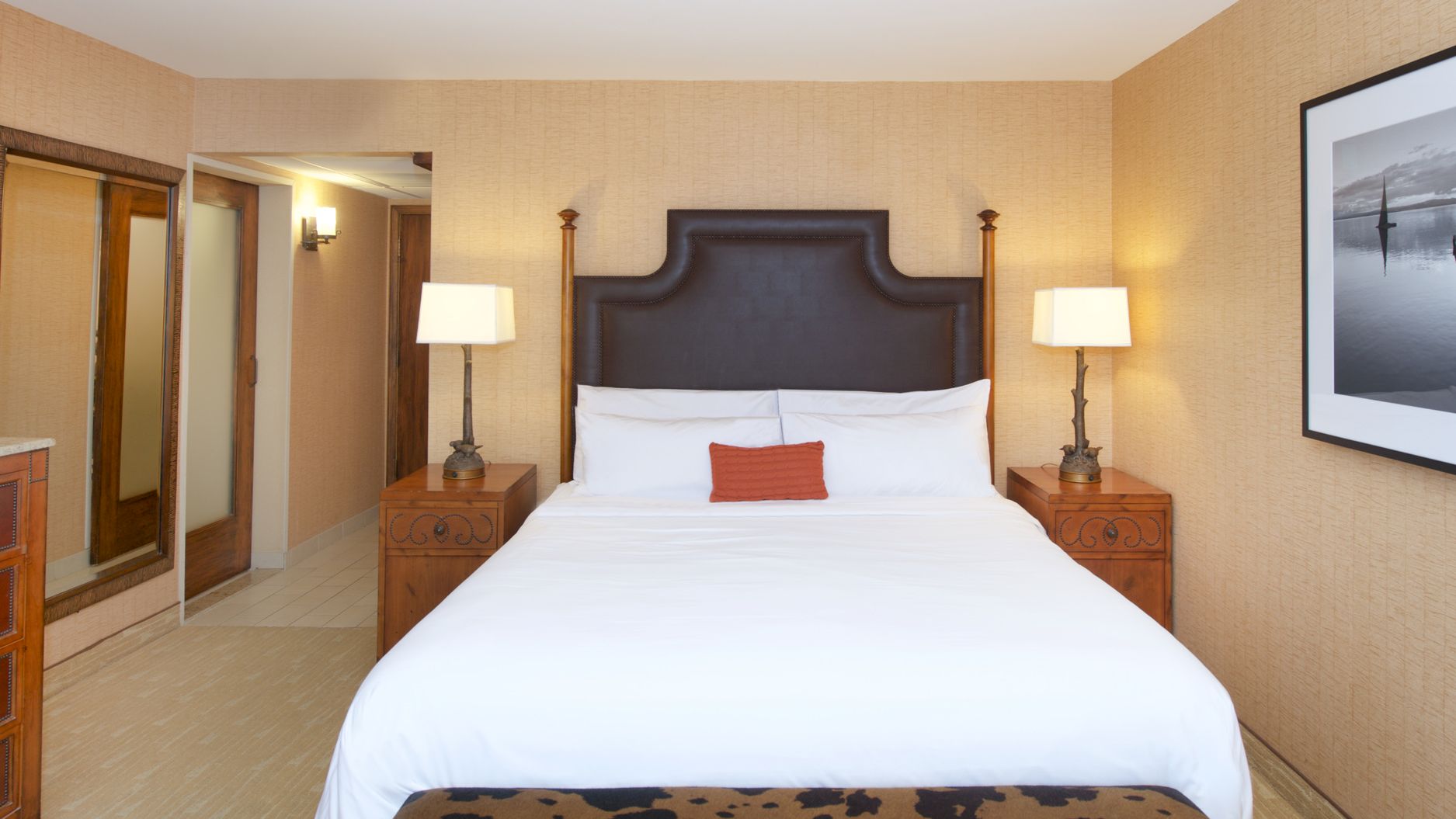 A neat hotel bedroom with a king-size bed, bedside lamps, wood dressers, and framed wall photos.