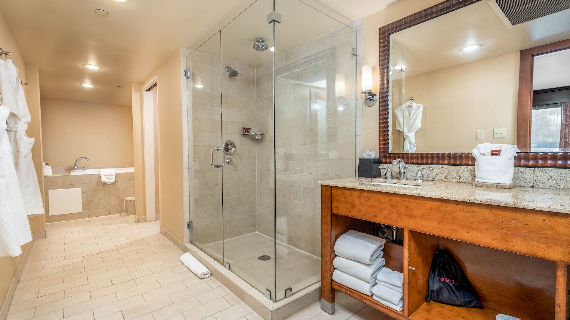 Modern hotel bathroom with a glass shower, tiled floor, and a granite vanity with towels and mirror.
