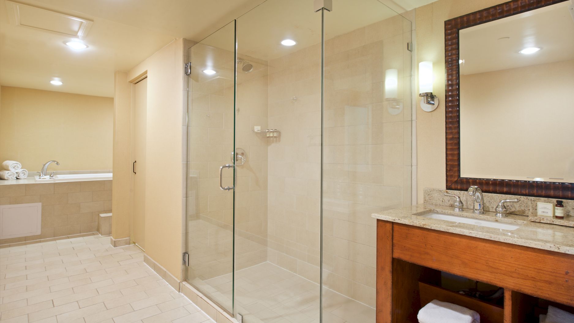 A bright modern bathroom with a glass shower, tiled walls, and a wooden vanity with double sinks.