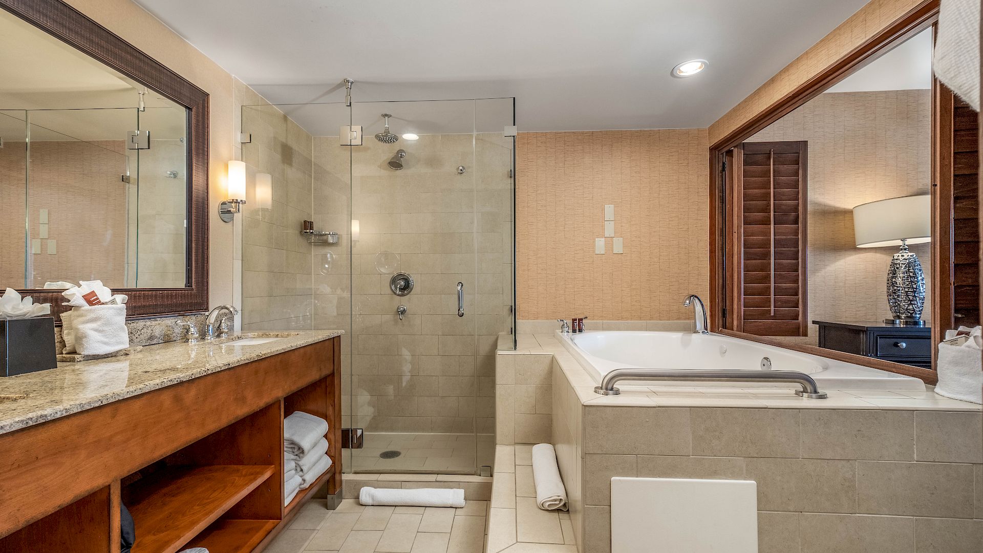 A modern bathroom with a glass shower, rainfall showerhead, granite vanity, and a soaking tub under warm lights.
