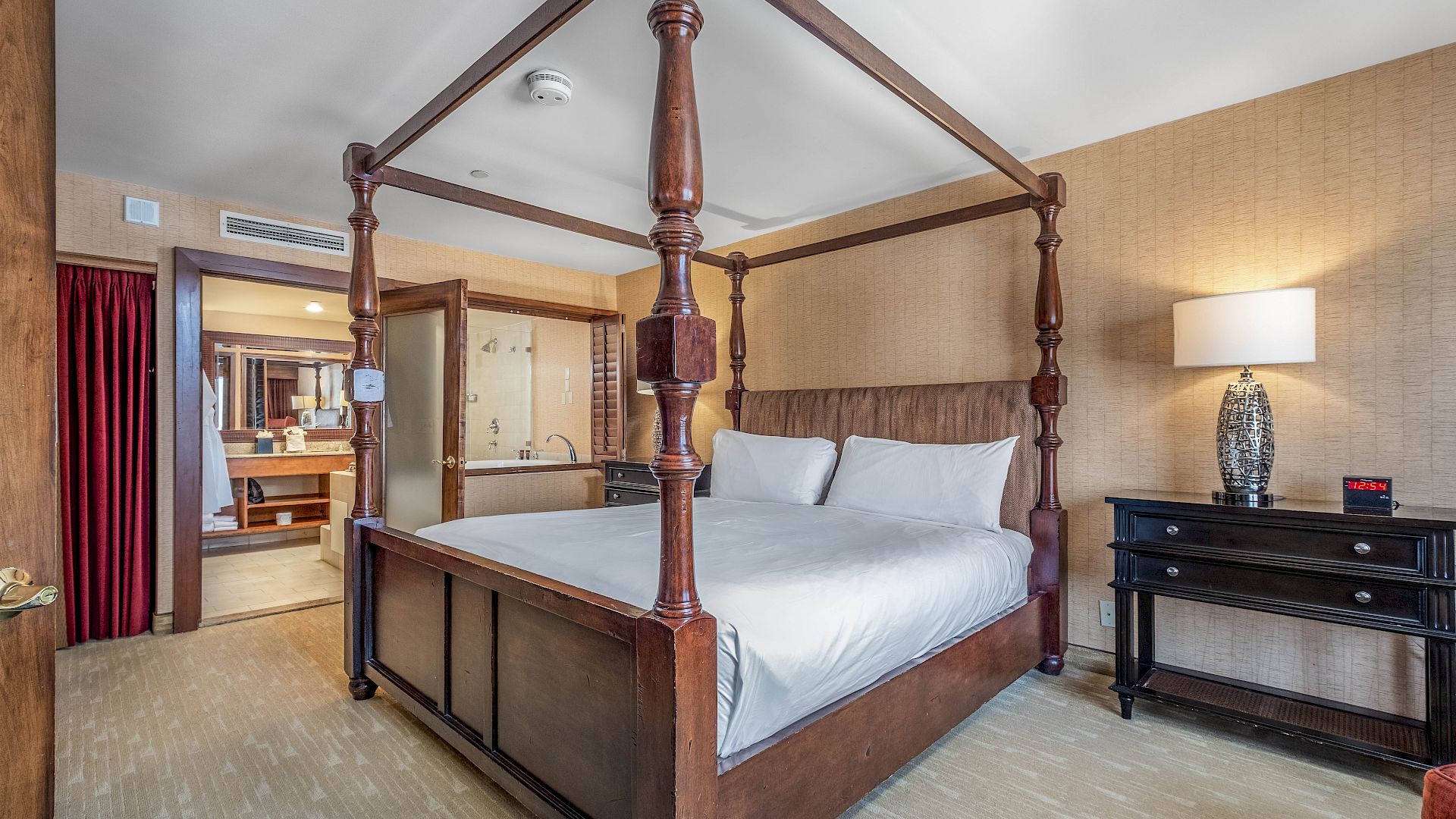 A hotel-style bedroom with a four-poster bed, white linens, wood panel walls, and bedside lamps.