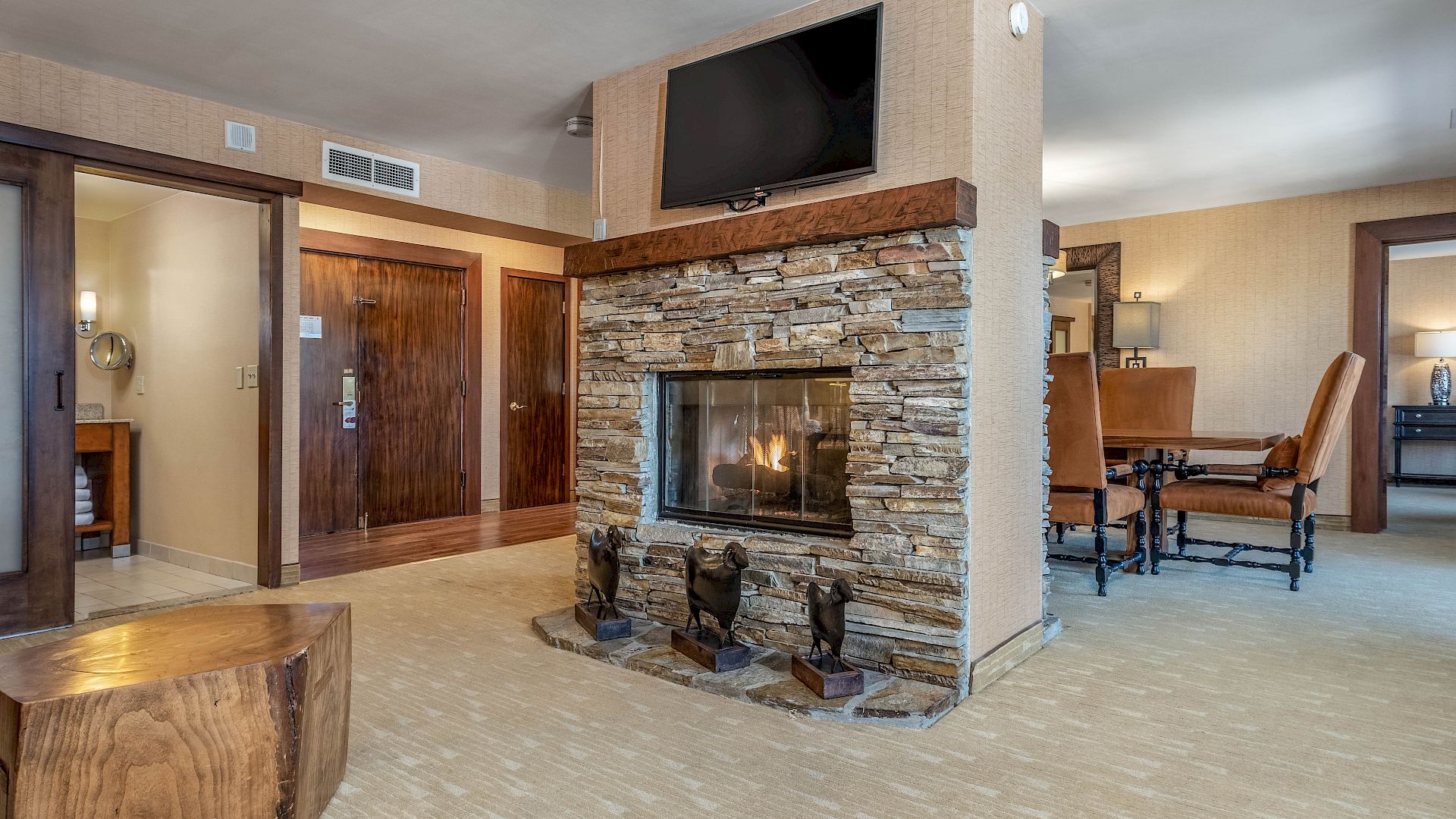 Indoor living room with a stone fireplace, mounted TV, wooden doors, and leather seating in warm light.