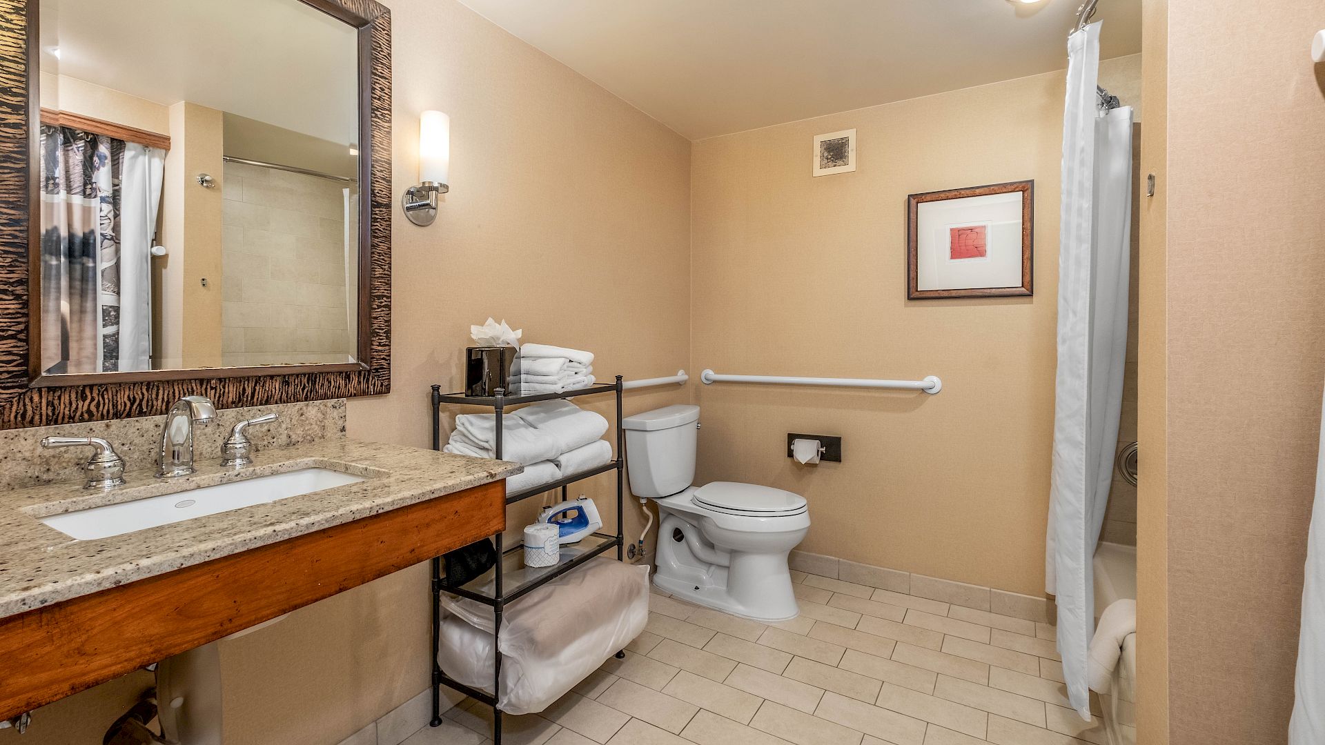 A clean hotel bathroom with a granite sink, large mirror, toilet, tub/shower, and neatly folded towels.