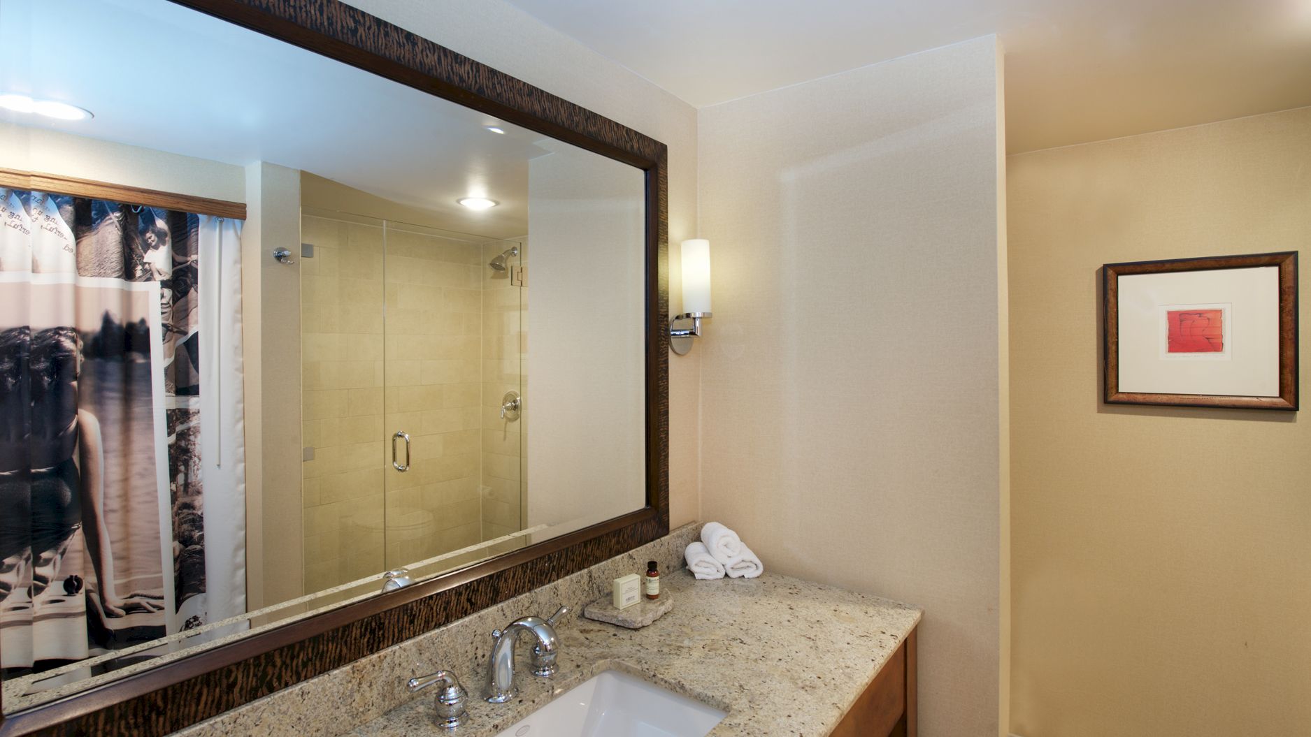 Bathroom with a granite sink, mirrors, towel stack, framed wall art, and a glass shower area with a curtain.