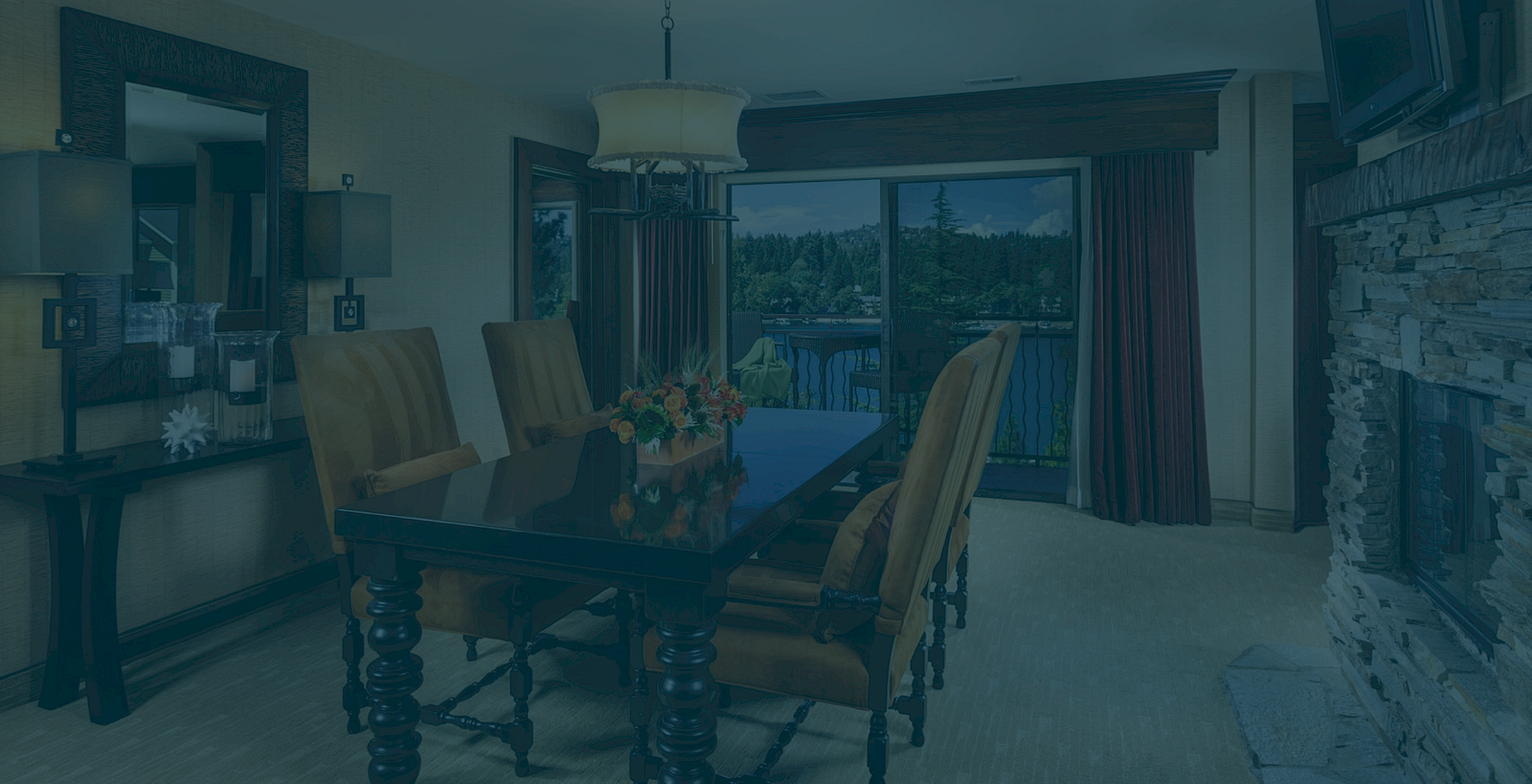 A cozy dining room with a dark table and chairs, a chandelier, and large windows showing trees and distant mountains.