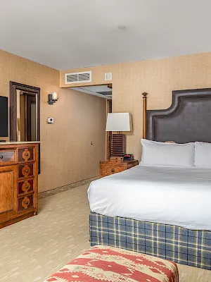 A hotel bedroom with a large bed, wood headboard, and a dresser cabinet holding a flat-screen TV.