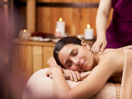 A woman lies on a massage table while a therapist gives a relaxing head and shoulder massage in a spa setting.