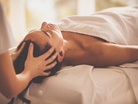 A relaxing massage session, with a woman lying on a bed while a therapist massages her shoulders and neck.