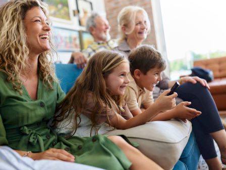 A family rides together, smiling as a woman and children look at a phone in a bright living-room style seating area.