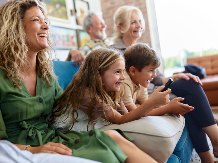 A family rides together, smiling as a woman and children look at a phone in a bright living-room style seating area.