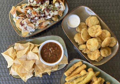 Overhead view of loaded nachos with sour cream, bacon bits, and chives, plus tortilla chips, fries, and dipping sauces.