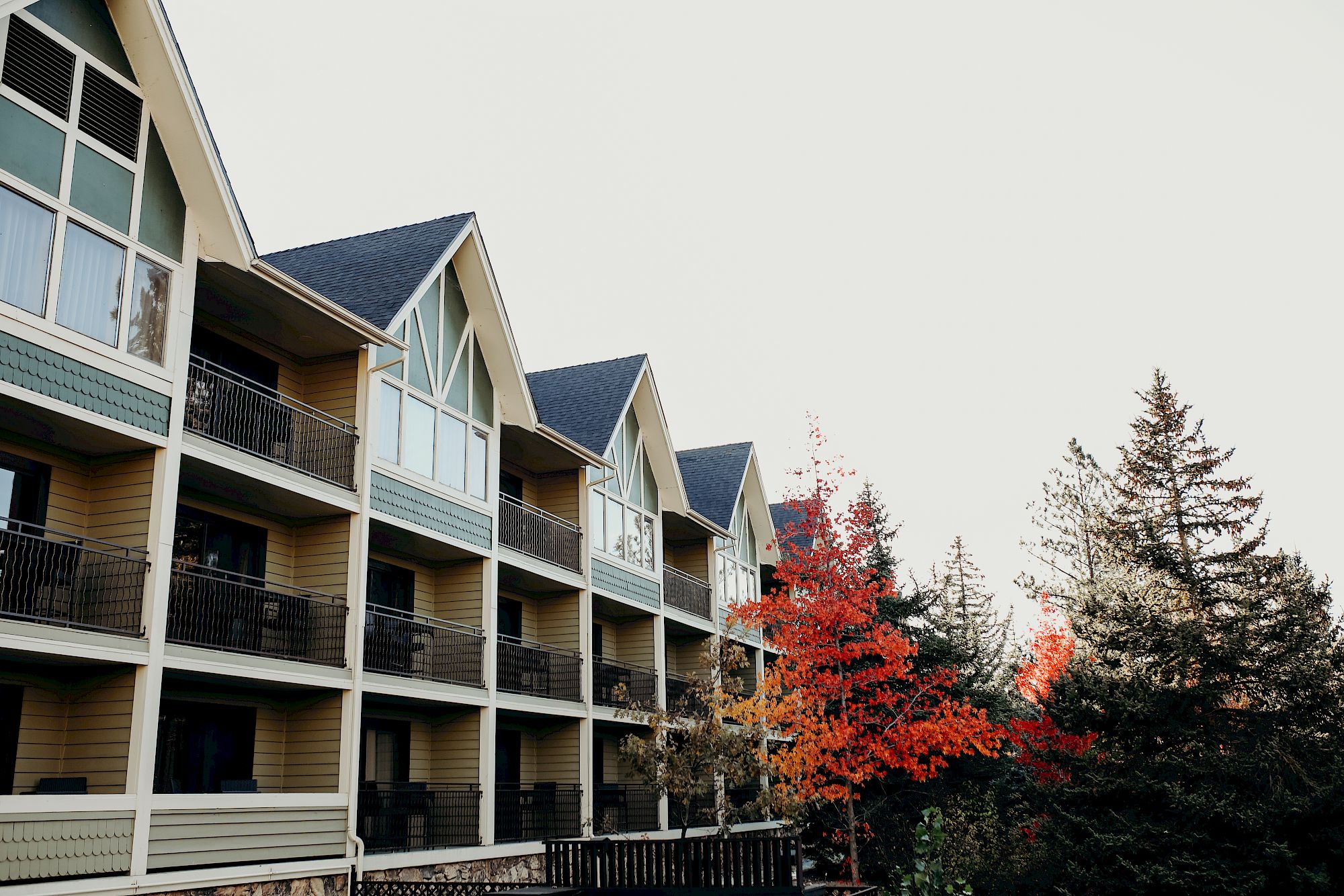 A multi-story townhouse with balconies and dark shingles, with bright red-orange autumn trees against a pale sky.